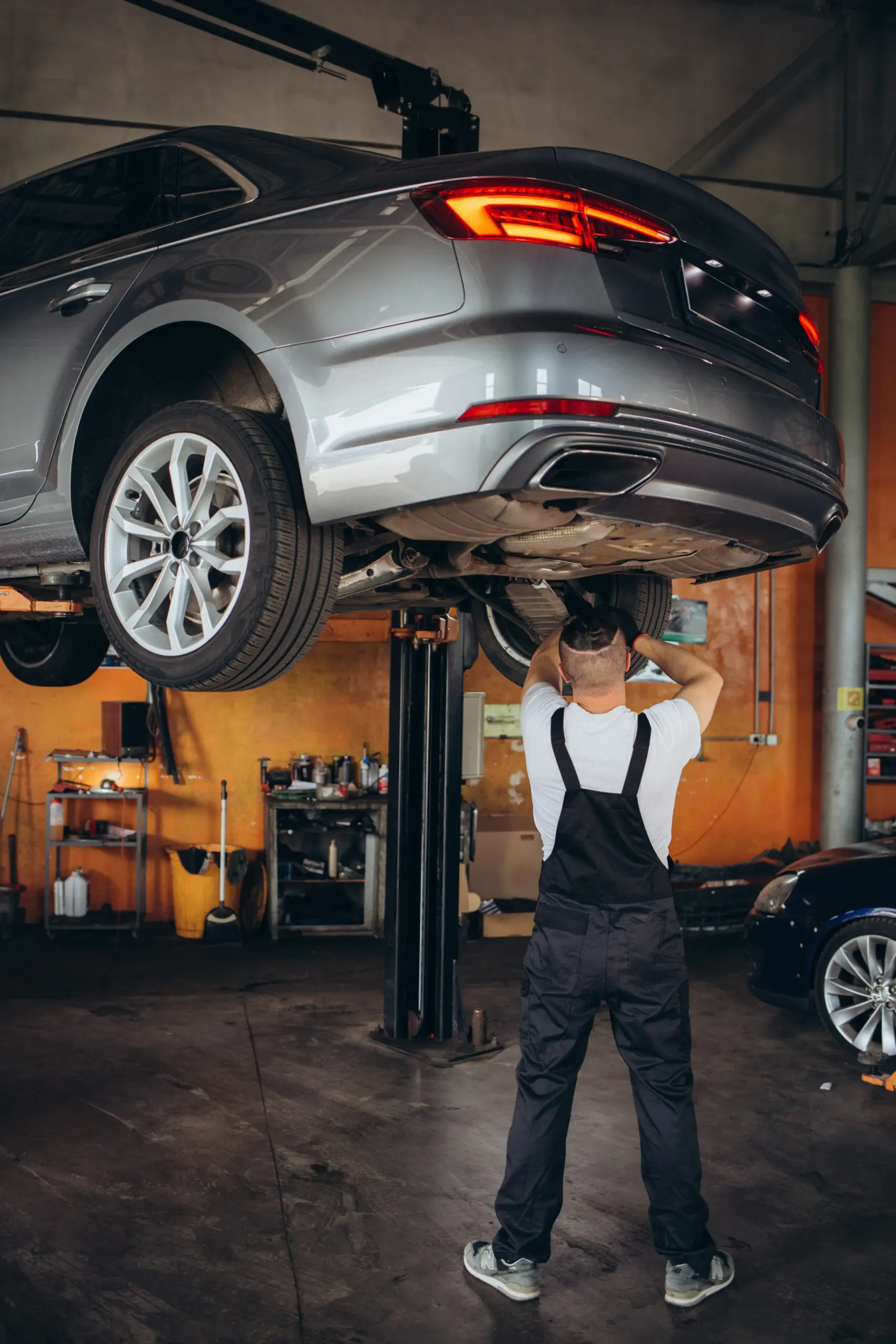 Mechanic working under a gray car on a hydraulic lift